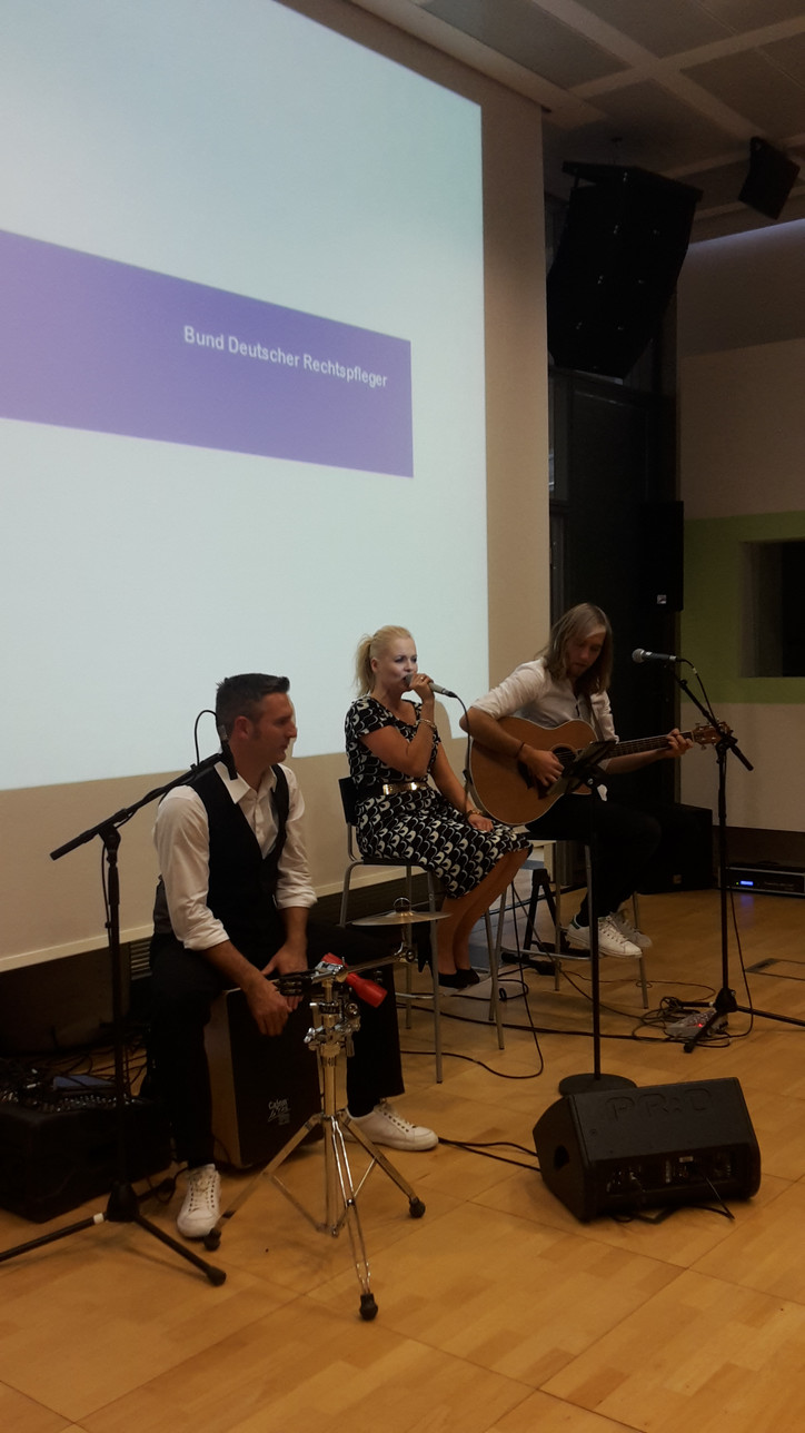 Musik zum Bundesrechtspflegertag 2016 Drei Musiker (Percussion, Gesang, Gitarre) performen in einem Raum vor Publikum