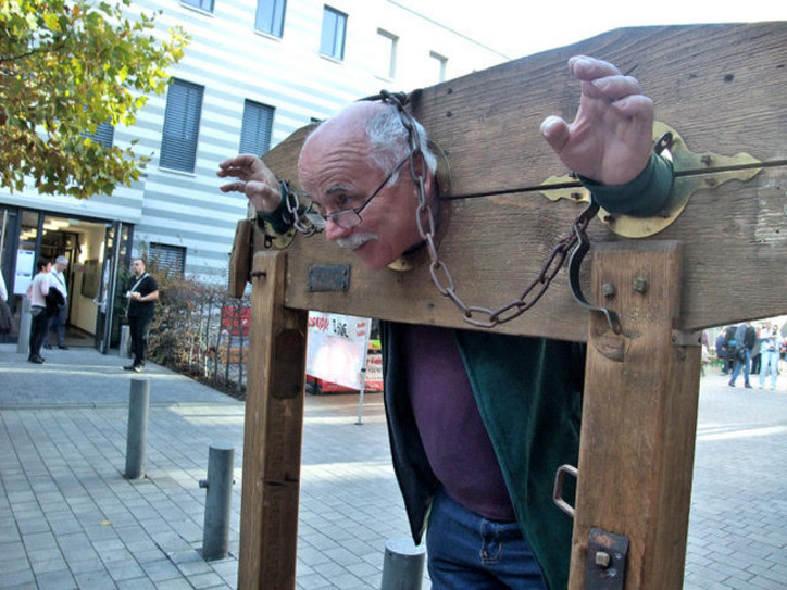 Vor den Pranger gestellt Ein Mann eingespannt in einem altertümlichen Pranger als Fotomotiv